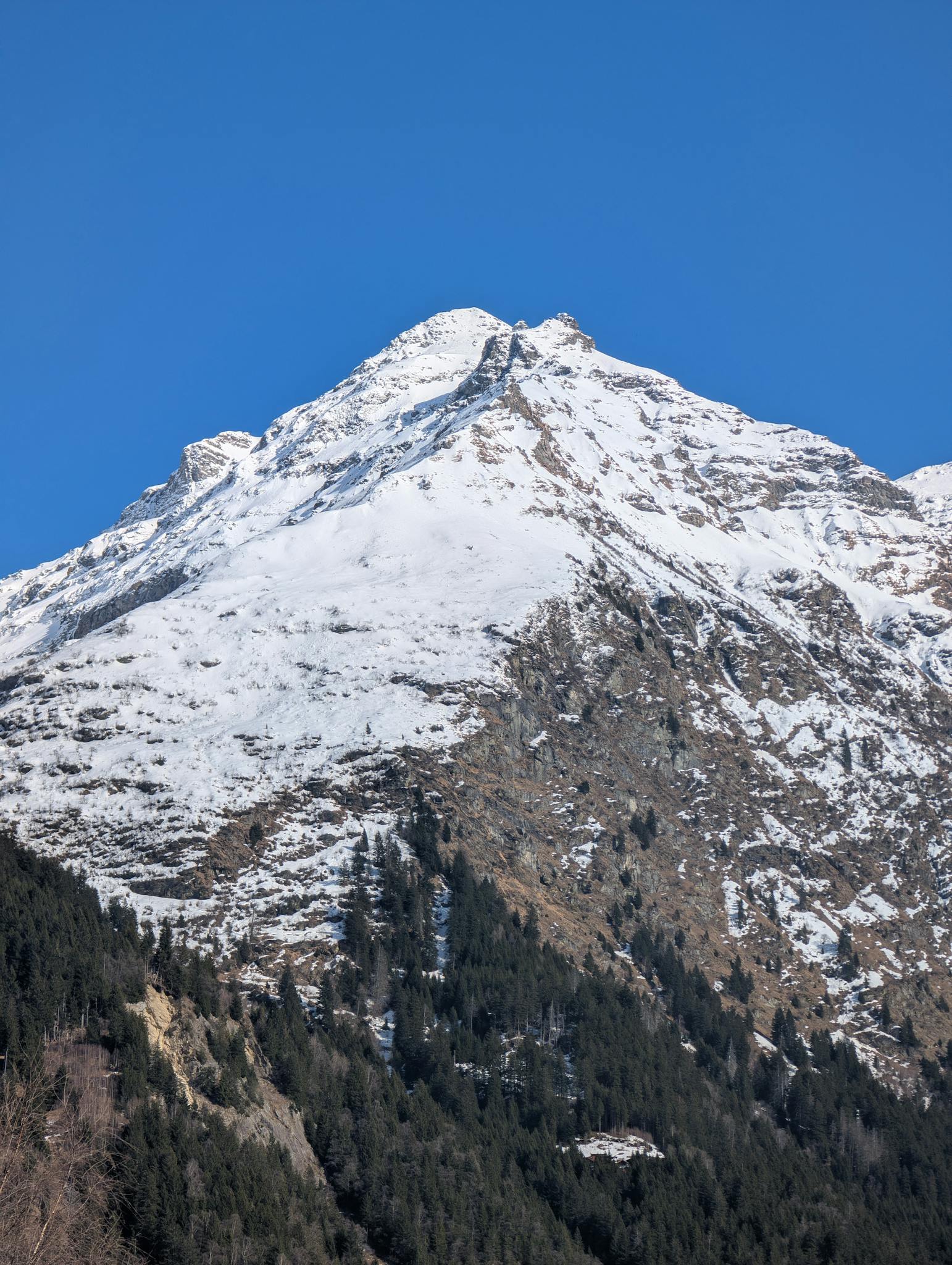 Snow-covered mountain peak piercing a clear blue sky, captured in daylight.