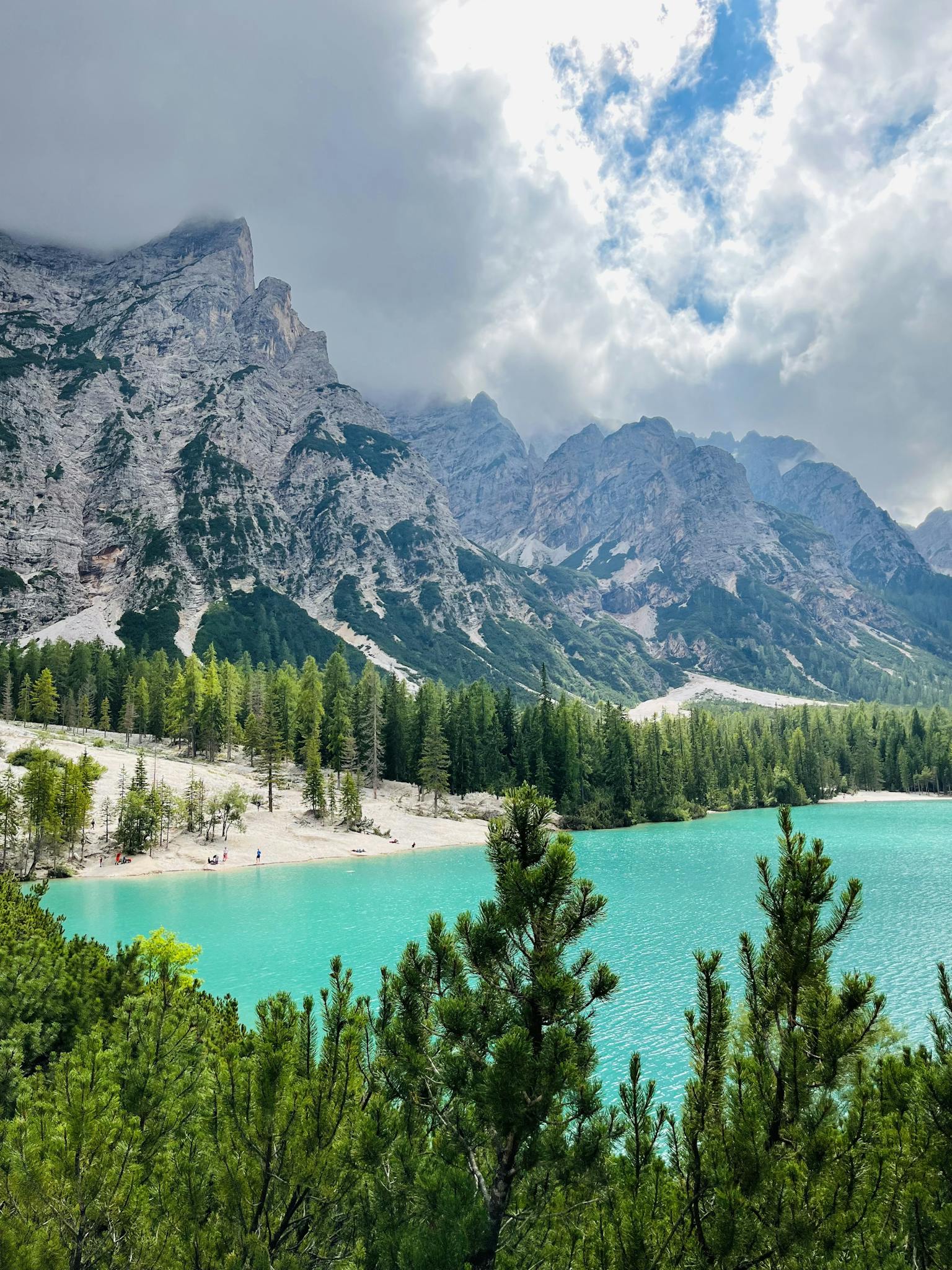 Stunning view of a turquoise alpine lake surrounded by rugged mountains and conifer trees.